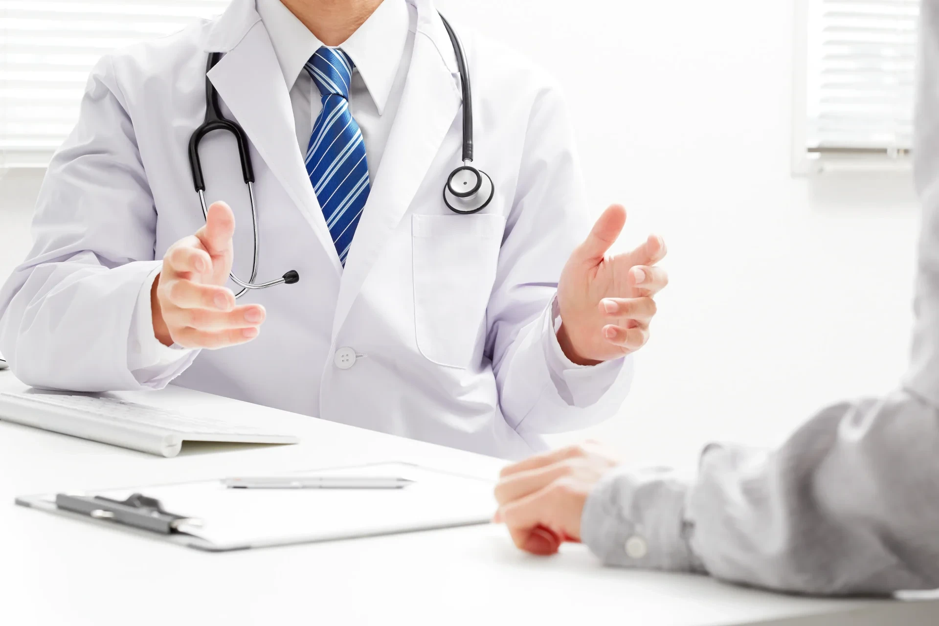 Arzt in Kittel und Stethoskop spricht mit unkenntlichem Patienten