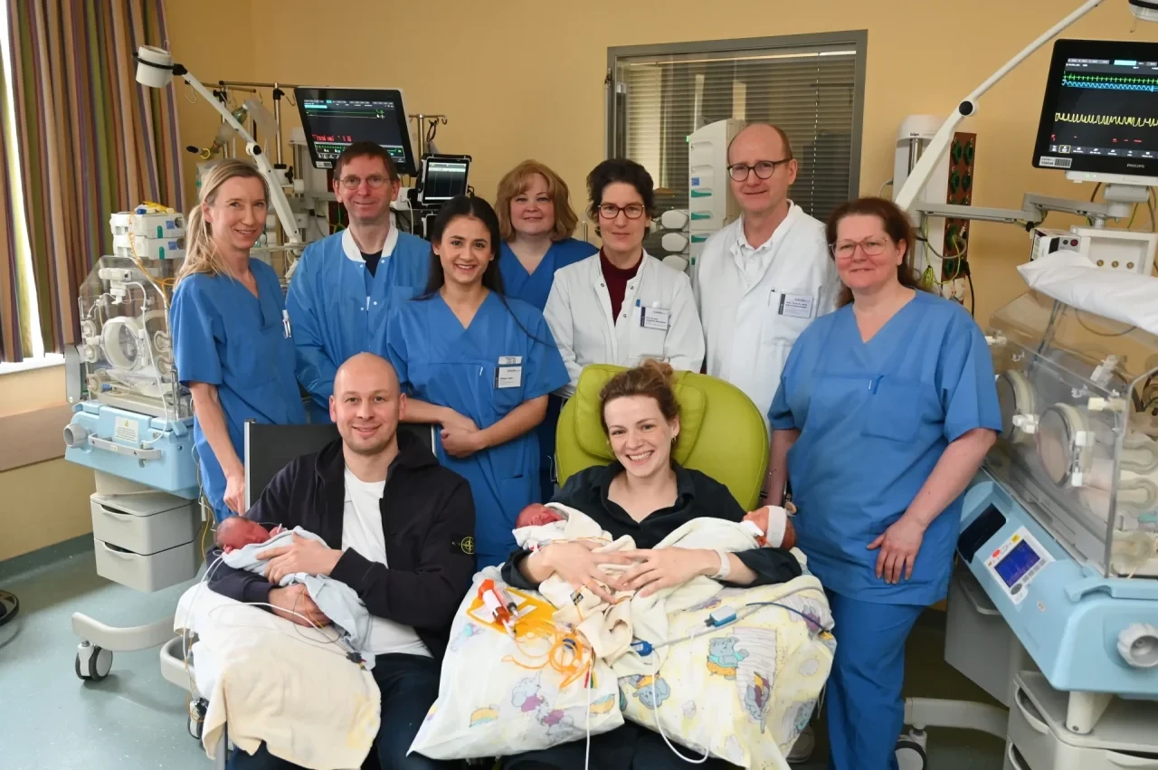 Die Eltern Mara (v.r.) und Max Deboer (v.l.) halten die Drillingsschwestern Klara, Romy und Jette (vorne l-r) auf dem Arm. Mit der Familie freuen sich aus dem Perinatalzentrum: Silke Beuse (Fachkinderkrankenschwester), Volkmar Kunde (Oberarzt auf der Frühgeborenenintensivstation), Hebamme Eliftara Camli, Susanne Auster (Pflegerische Leitung der Frauenklinik), Constanze Banz-Jansen (Chefärztin der Frauenklinik), Eckard Hamelmann (Ärztlicher Direktor des Kinderzentrums) und Michael Mülligans (Leitende Hebamme). Eineiige Drillinge sind ein extrem seltenes Ereignis.
