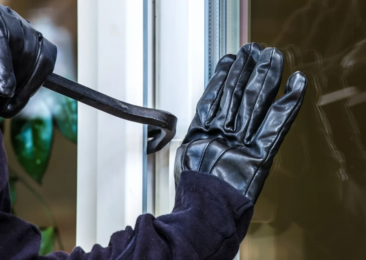 Einbrecher mit Handschuhen und Brechstange bricht Fenster auf
