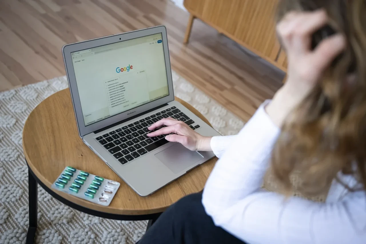 Frau sitzt besorgt vor einem Laptop mit geöffneter Google-Suche, daneben liegen Medikamentenblister – Symbolbild für Cyberchondrie und Online-Symptomsuche.