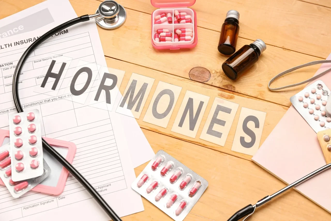 Buchstaben legen das Wort Hormone aus, umgeben von Tablettenblistern und einem Stethoskop