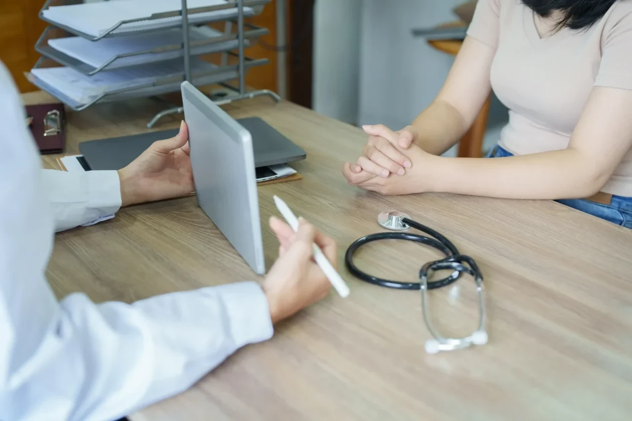 Arzt und Patientin sitzen sich gegenüber, Ärztin hält ein Tablet in der Hand
