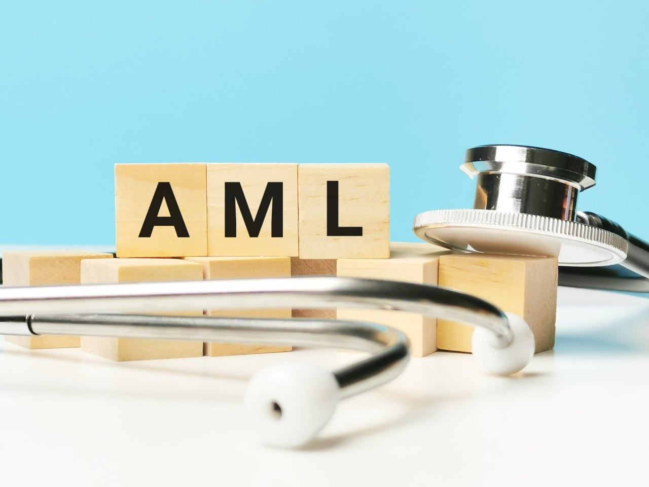 Holzwürfel mit der Aufschrift „AML“ liegen auf einer hellen Fläche, umgeben von einem Stetoskop