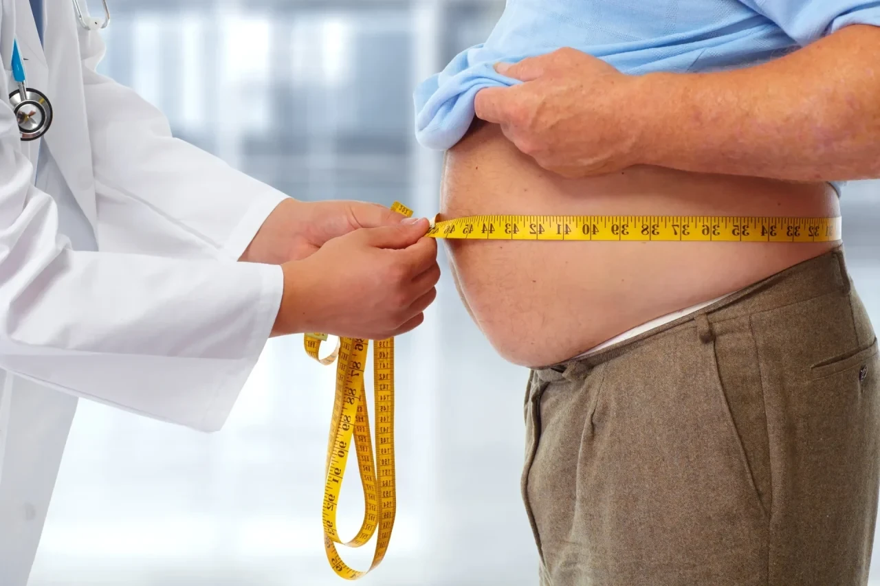 Arzt mit Maßband am Bauch eines übergewichtigen Patienten
