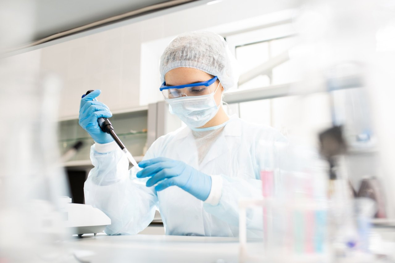 Laborantin mit Schutzkleidung und Maske hantiert mit Pipette