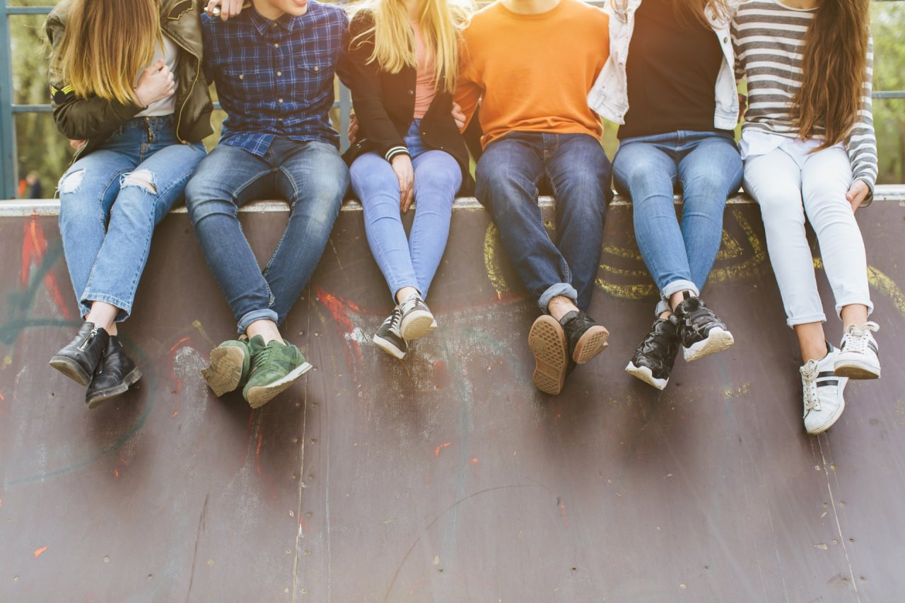 Sechs junge Menschen sitzen nebeneinander auf einer Mauer, ihre Beine baumeln herunter