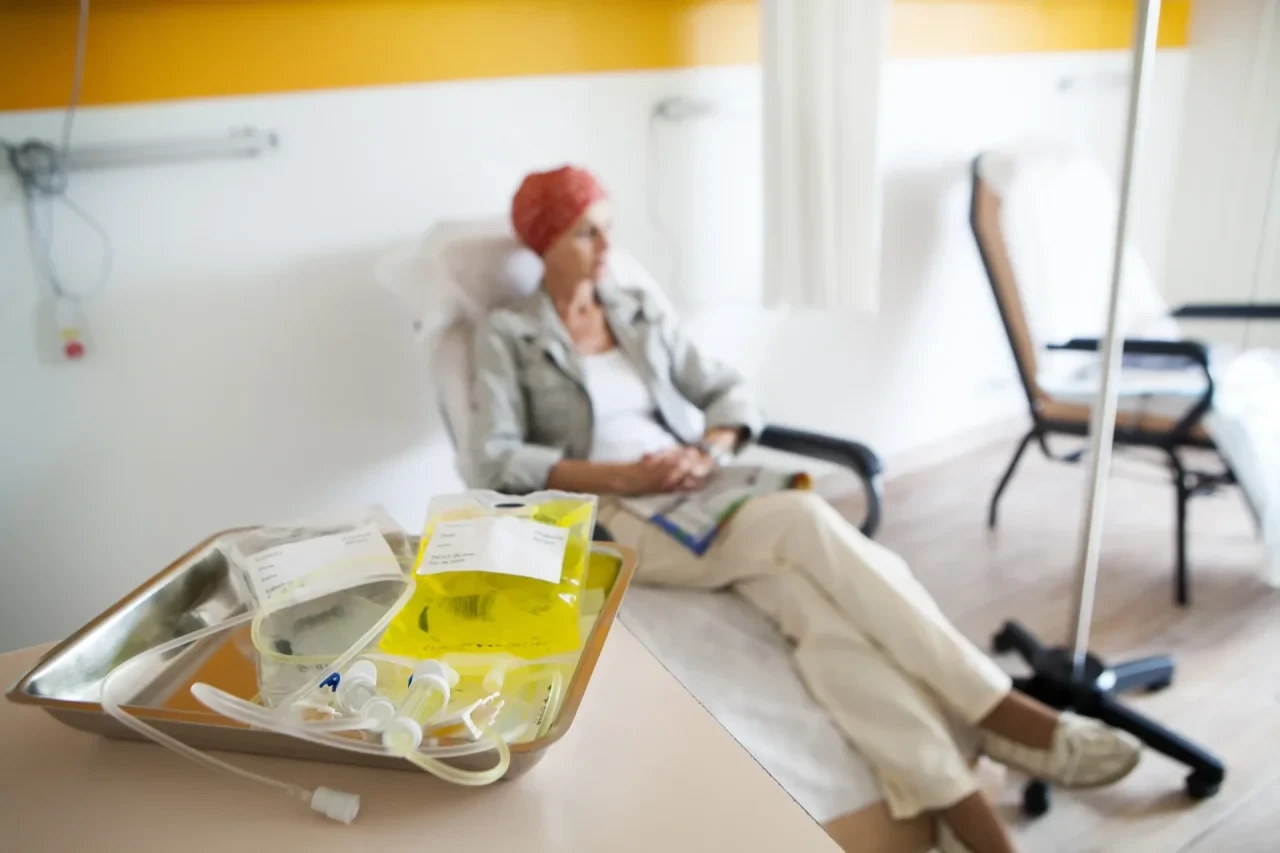 Ambulante Chemotherapie: Im Vordergrund liegen Chemotherapie-Infusionsmaterialien auf einem Tablett, im Hintergrund sitzt eine Patientin mit Kopftuch entspannt in einem Behandlungsstuhl während der Therapie.