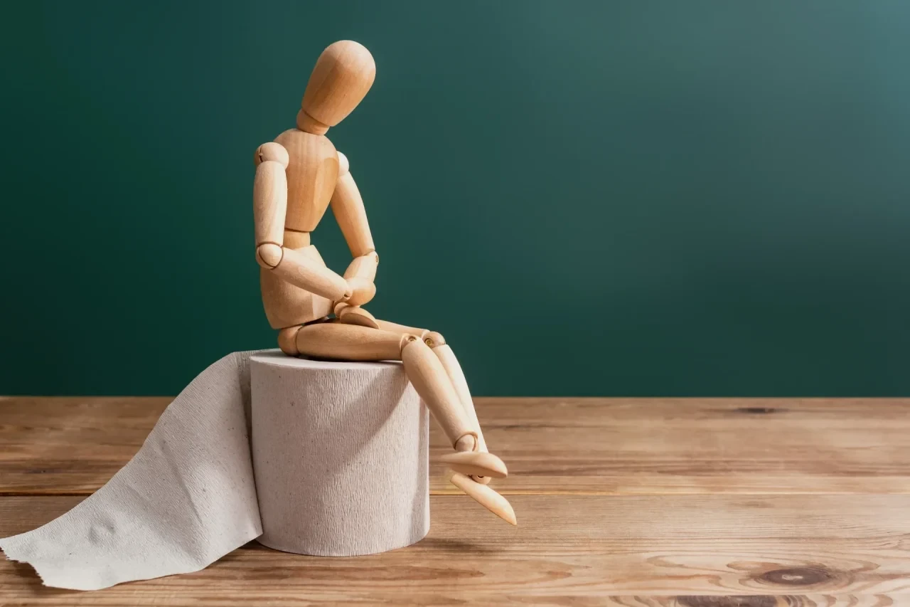 Holzfigur sitzt auf einer Rolle Toilettenpapier wegen Verstopfung