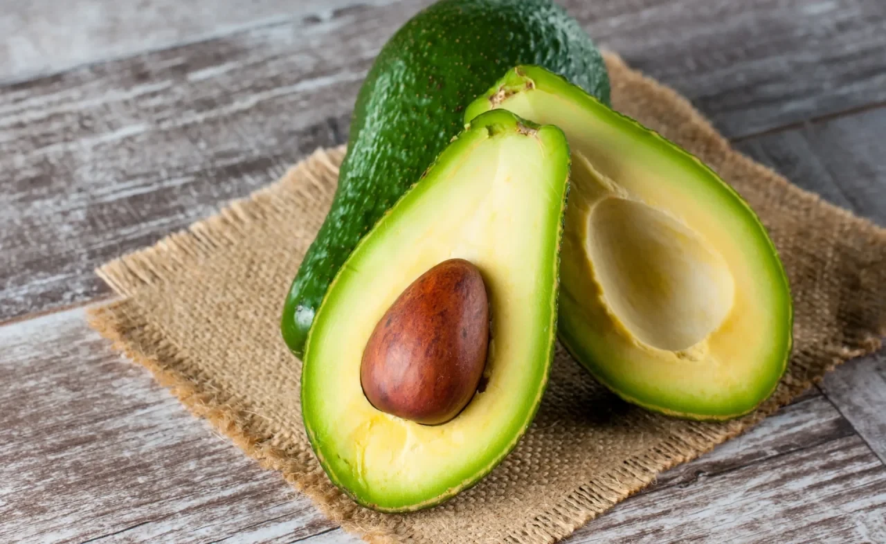 Aufgeschnittene Avocadohälften mit Kern und grünem Fruchtfleisch liegen auf einer groben Stoffunterlage auf einem Holztisch.