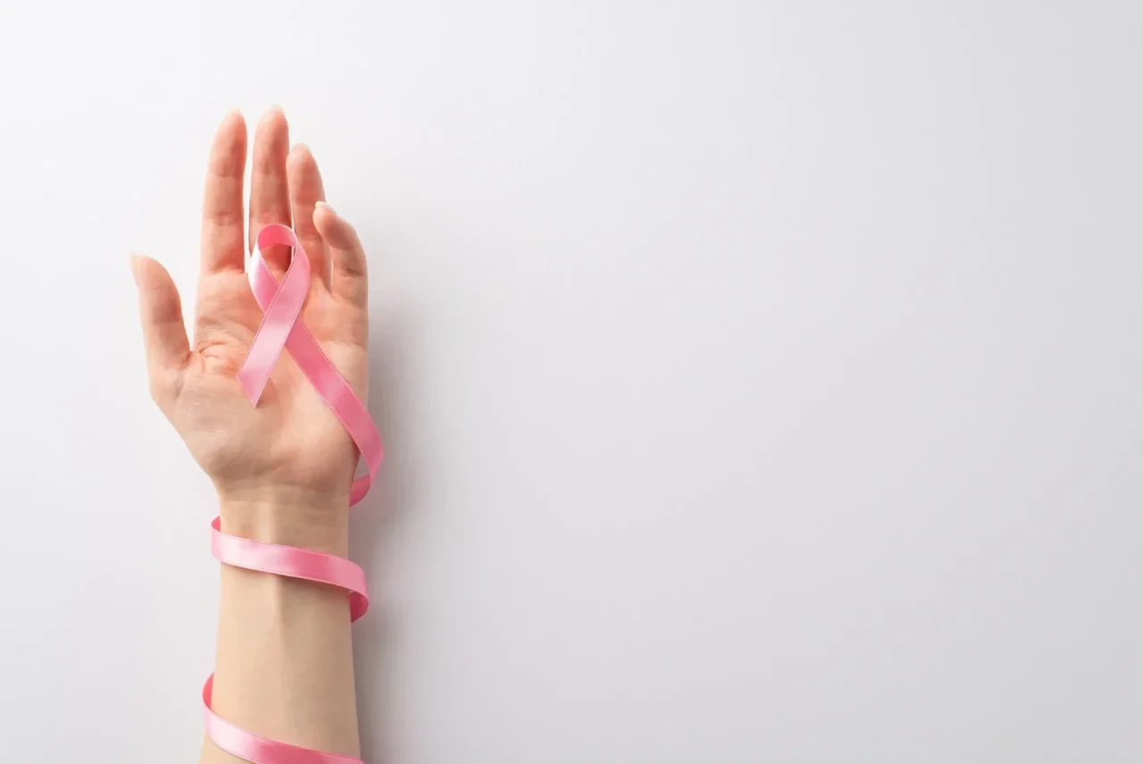 Eine erhobene Hand hält eine rosafarbene Schleife, das internationale Symbol für Brustkrebsbewusstsei.