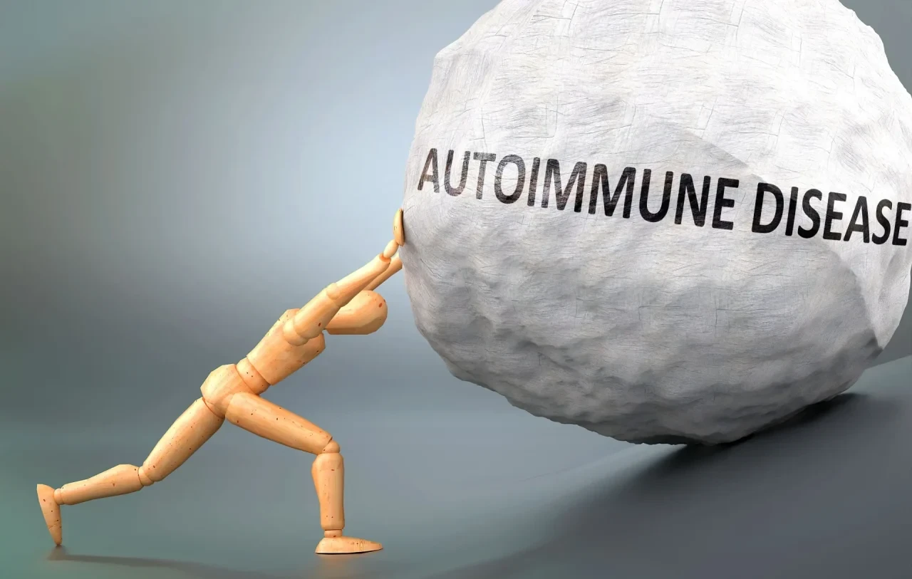 Eine stilisierte Holzfigur stemmt sich mit ausgestreckten Armen und gebeugtem Körper gegen eine große graue Kugel, auf der in Großbuchstaben „AUTOIMMUNE DISEASE“ steht.