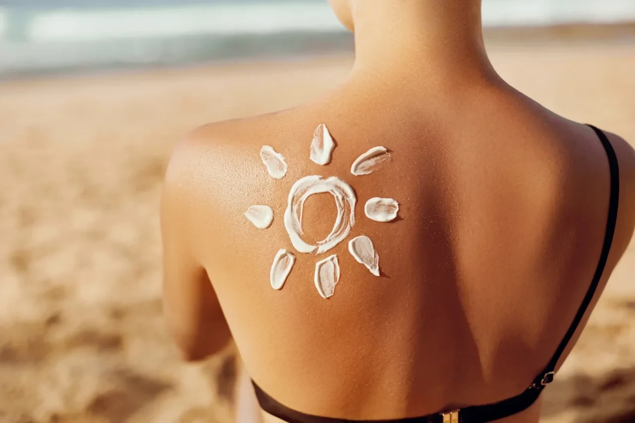 Rücken einer Frau am Strand mit aufgemalter Sonne aus Sonnencreme