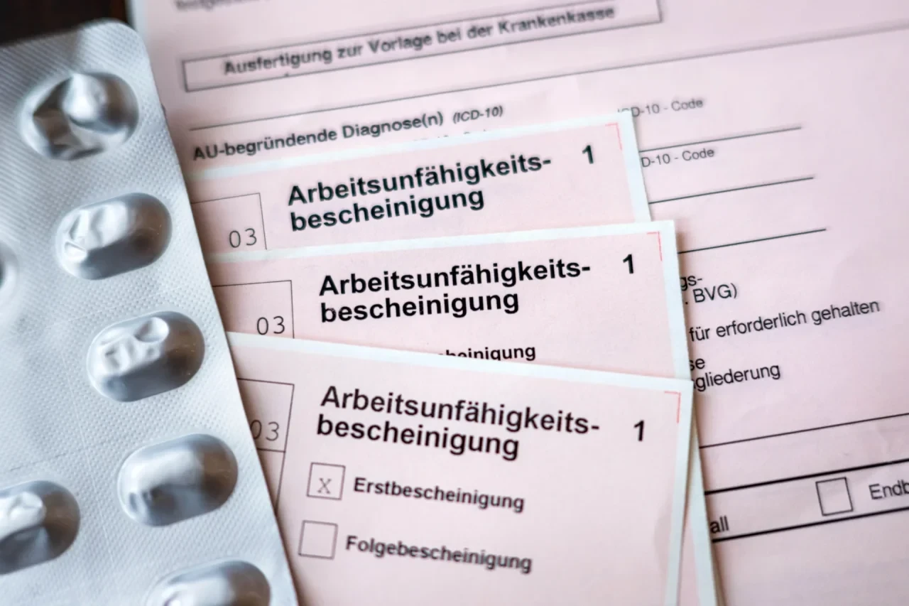 Mehrere Formulare zur Arbeitsunfähigkeitsbescheinigung liegen neben einem Blister mit Tabletten auf einem Tisch.