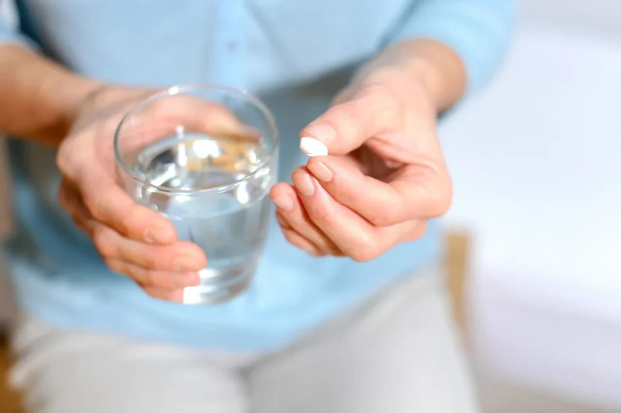 Ältere Frau nimmt eine Tablette mit einem Glas Wasser ein