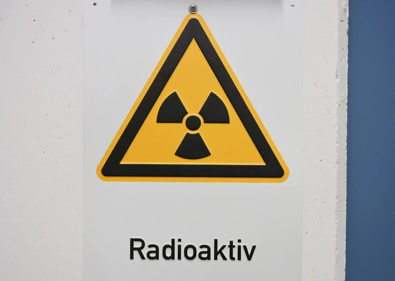 Gelbes dreieckiges Warnschild mit schwarzem Strahlensymbol und der Aufschrift „Radioaktiv“.