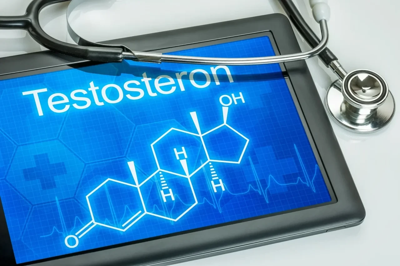 Ein Tablet auf weißem Untergrund zeigt auf blauem Bildschirm die chemische Strukturformel von Testosteron und das Wort „Testosteron“. Daneben liegt ein medizinisches Stethoskop.