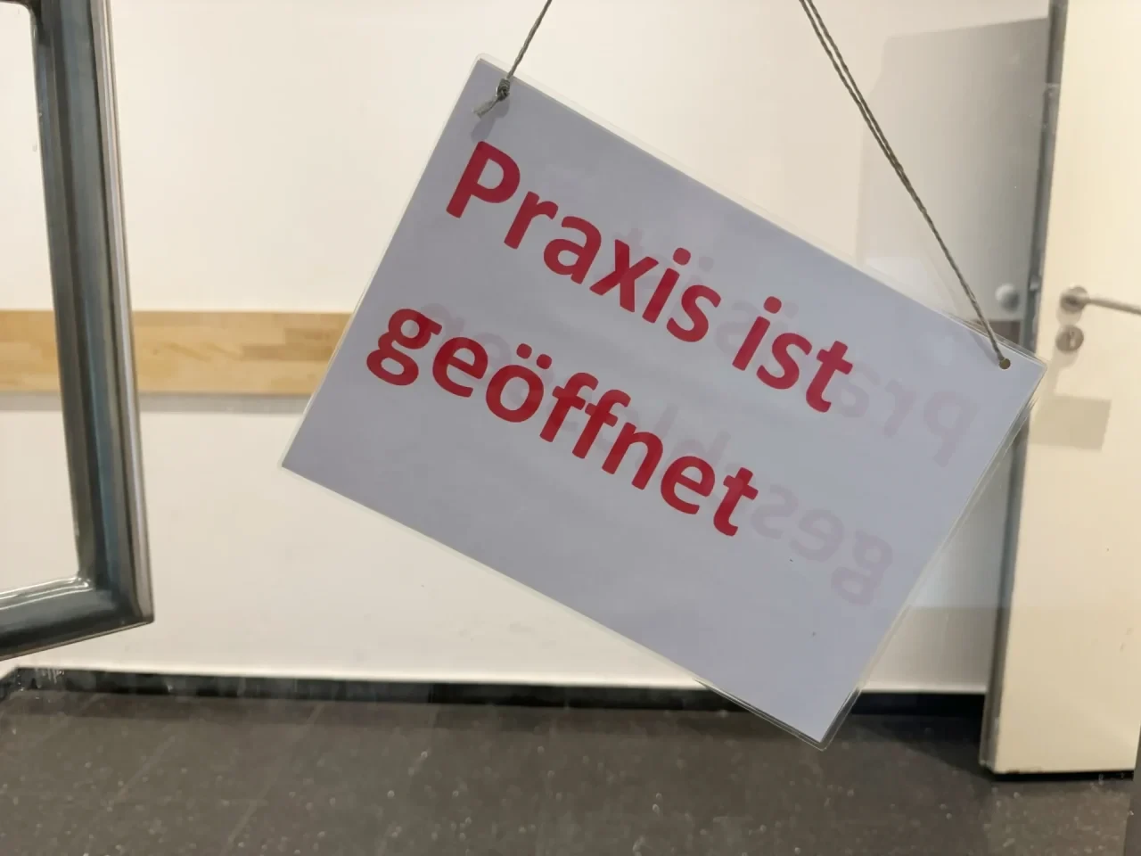 Ein Schild mit der Aufschrift „ Praxis ist geöffnet“ hängt an der Eingangstür einer Arztpraxis.