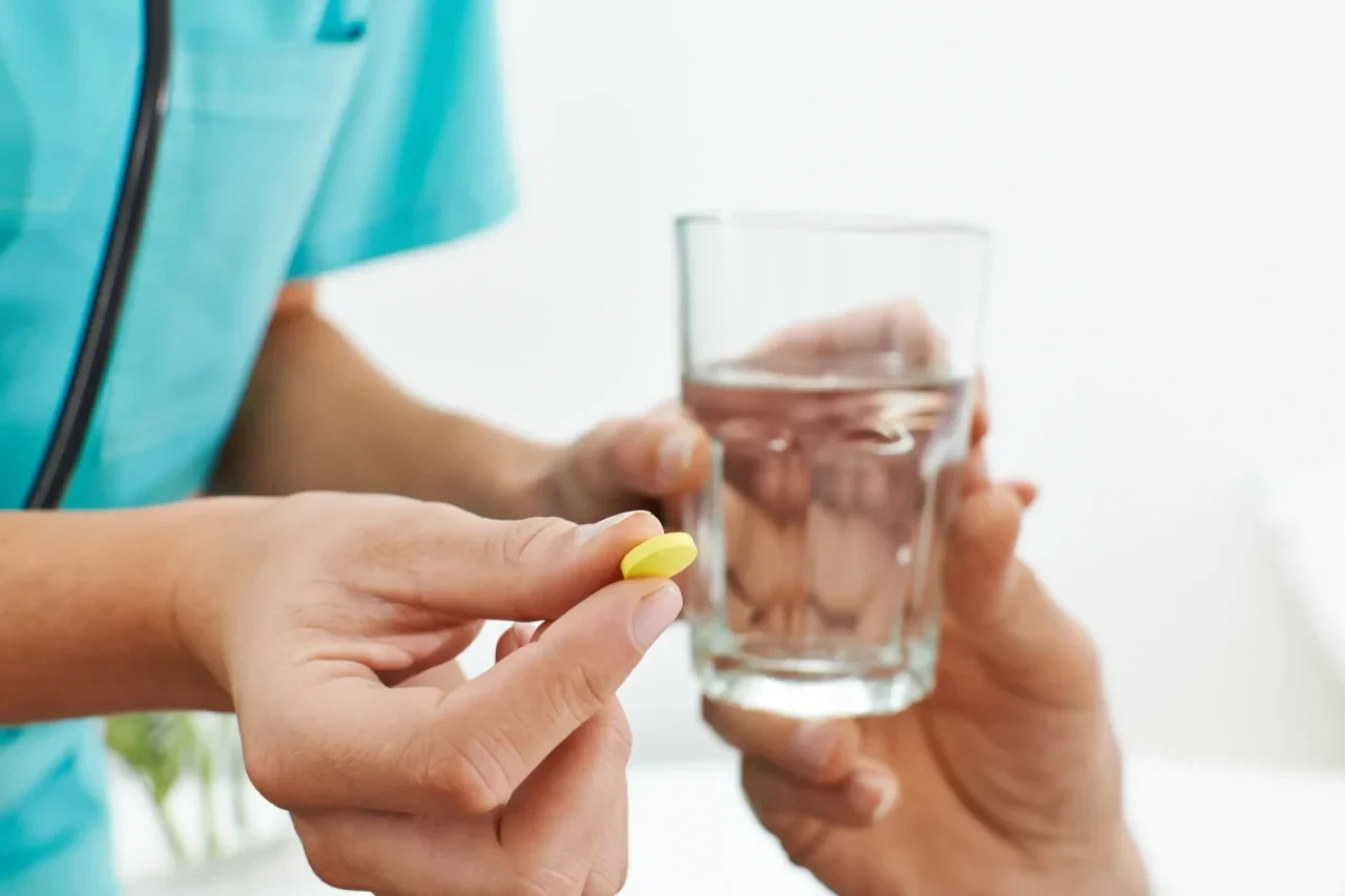 Tablette und Glas Wasser werden von einer Krankenschwester an einen Patienten gereicht