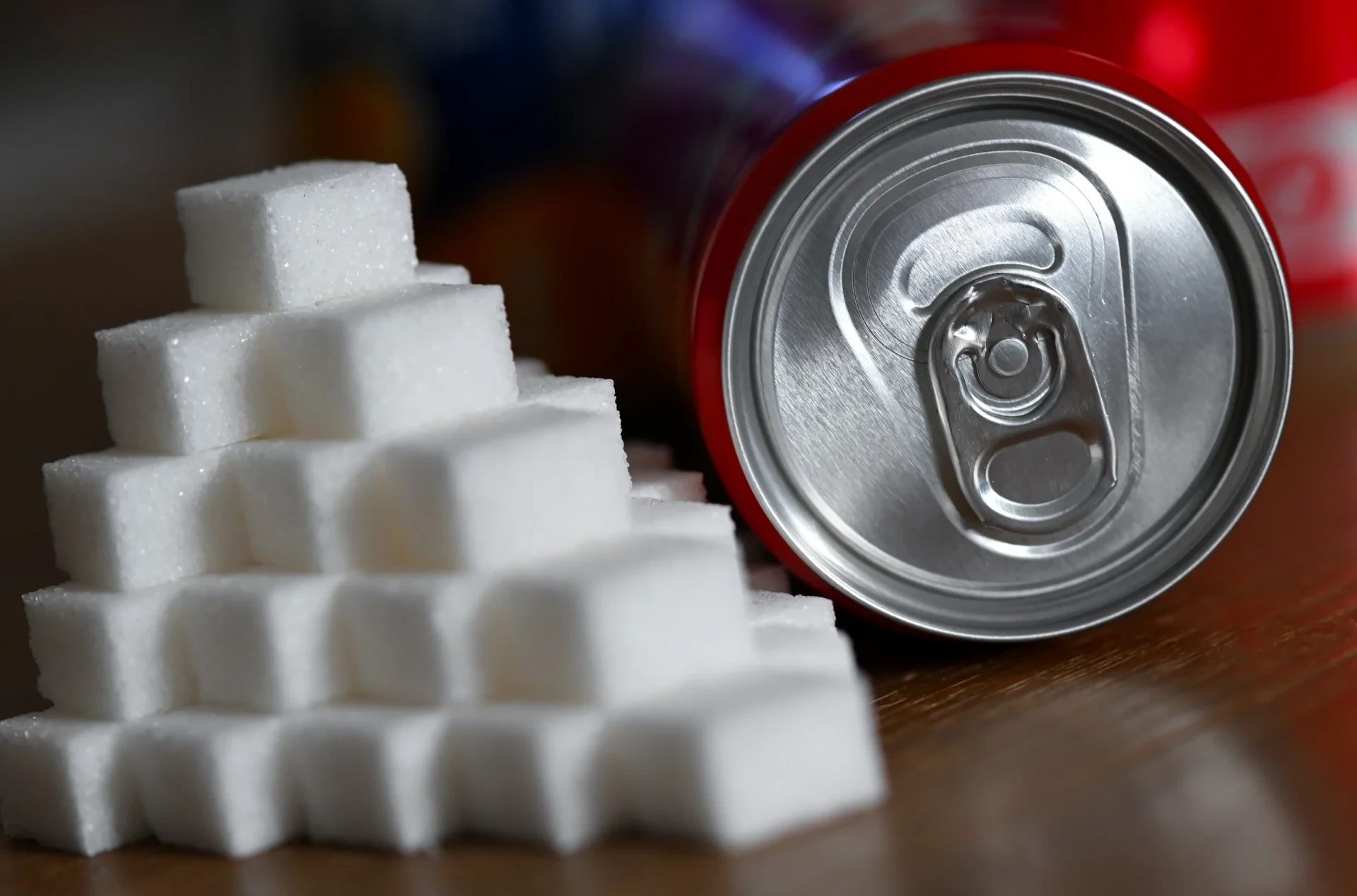 Eine Getränkedose mit einem Softdrink und zahlreiche Zuckerwürfel liegen auf einem Tisch.