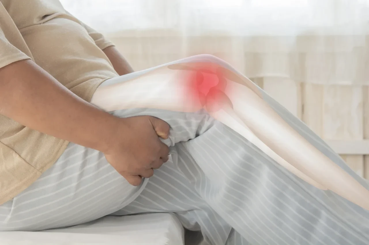 Person in sitzender Position hält sich das Knie; das Kniegelenk ist mit einer rot hervorgehobenen Schmerzzone dargestellt.