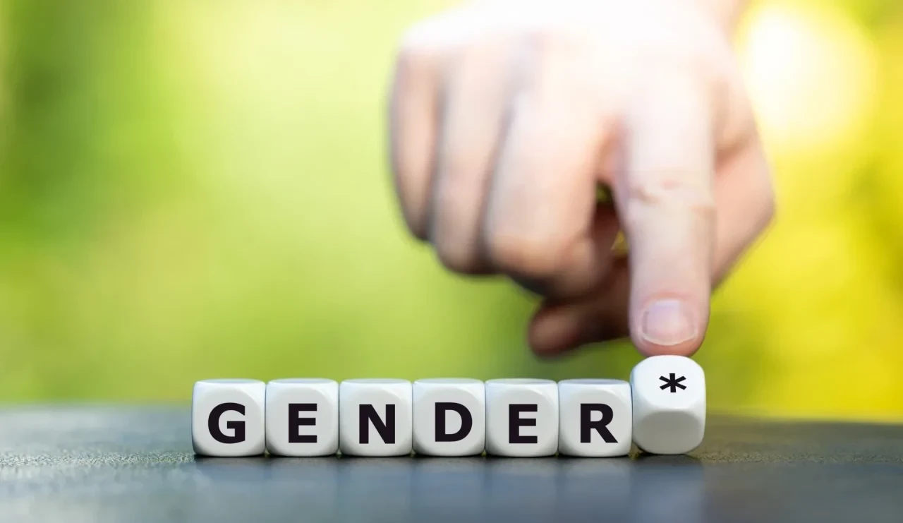 Nahaufnahme von weißen Würfeln mit dem Schriftzug „GENDER“. Eine Hand berührt den letzten Würfel mit einem Sternsymbol.