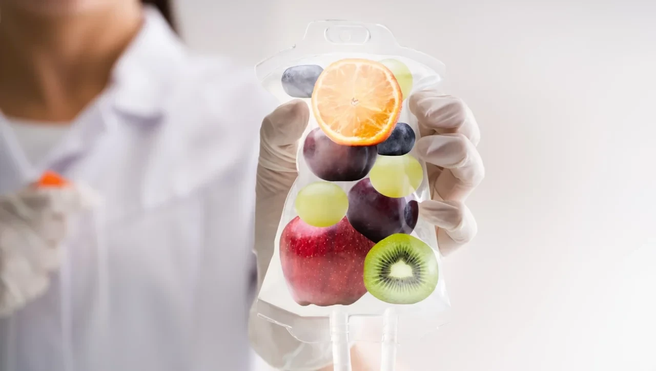 Ärztin in weißem Kittel hält Infusionsbeutel mit frischem Obst wie Orange, Apfel, Kiwi, Trauben und Pflaumen.