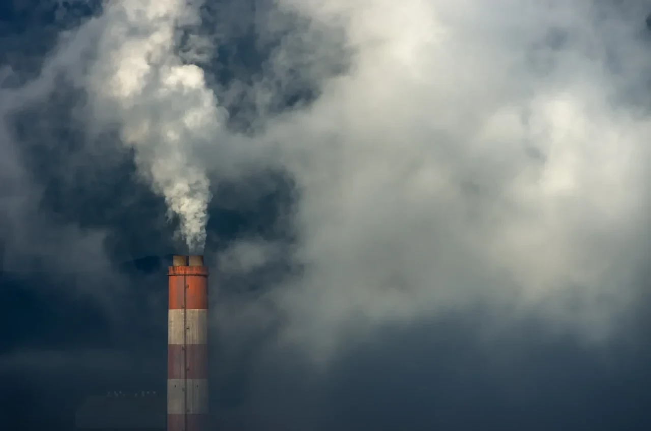 Rot-weiß gestreifter Industrieschornstein stößt dichte weiße Rauchwolken in einen bewölkten Himmel aus