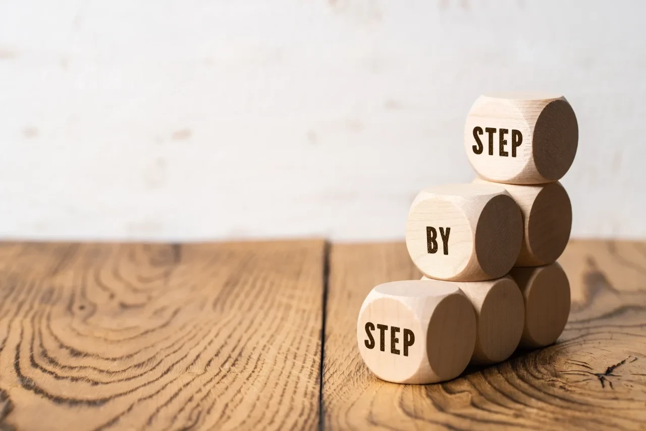 Drei gestapelte Holzwürfel mit der Aufschrift „Step by Step"