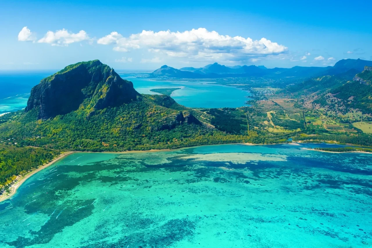 Luftaufnahme der Insel Mauritius mit dem markanten Berg Le Morne Brabant, türkisfarbenem Lagunenwasser und bergiger Küstenlandschaft im Indischen Ozean.