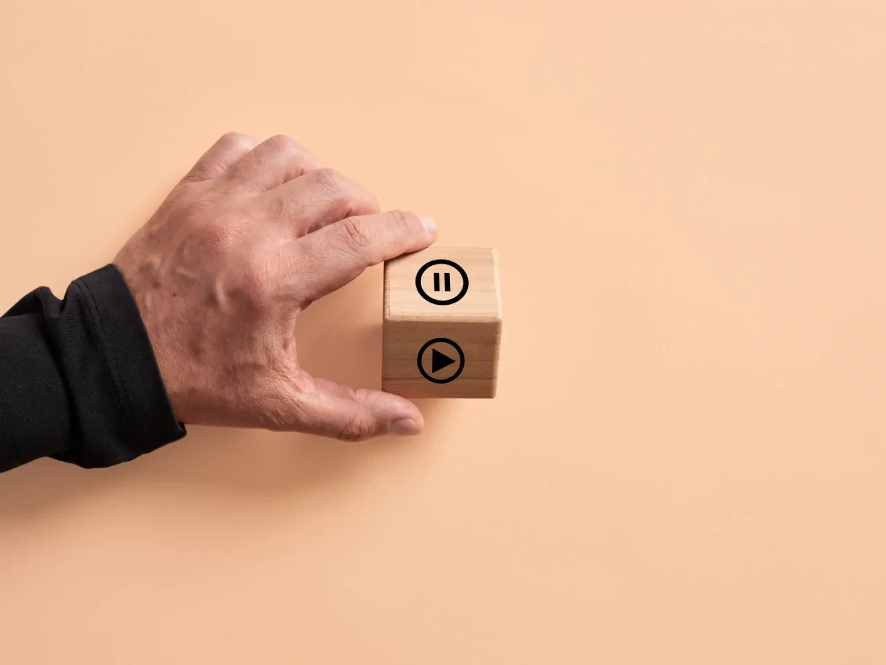 Hand hält Holzwürfel mit Pause- und Play-Symbol