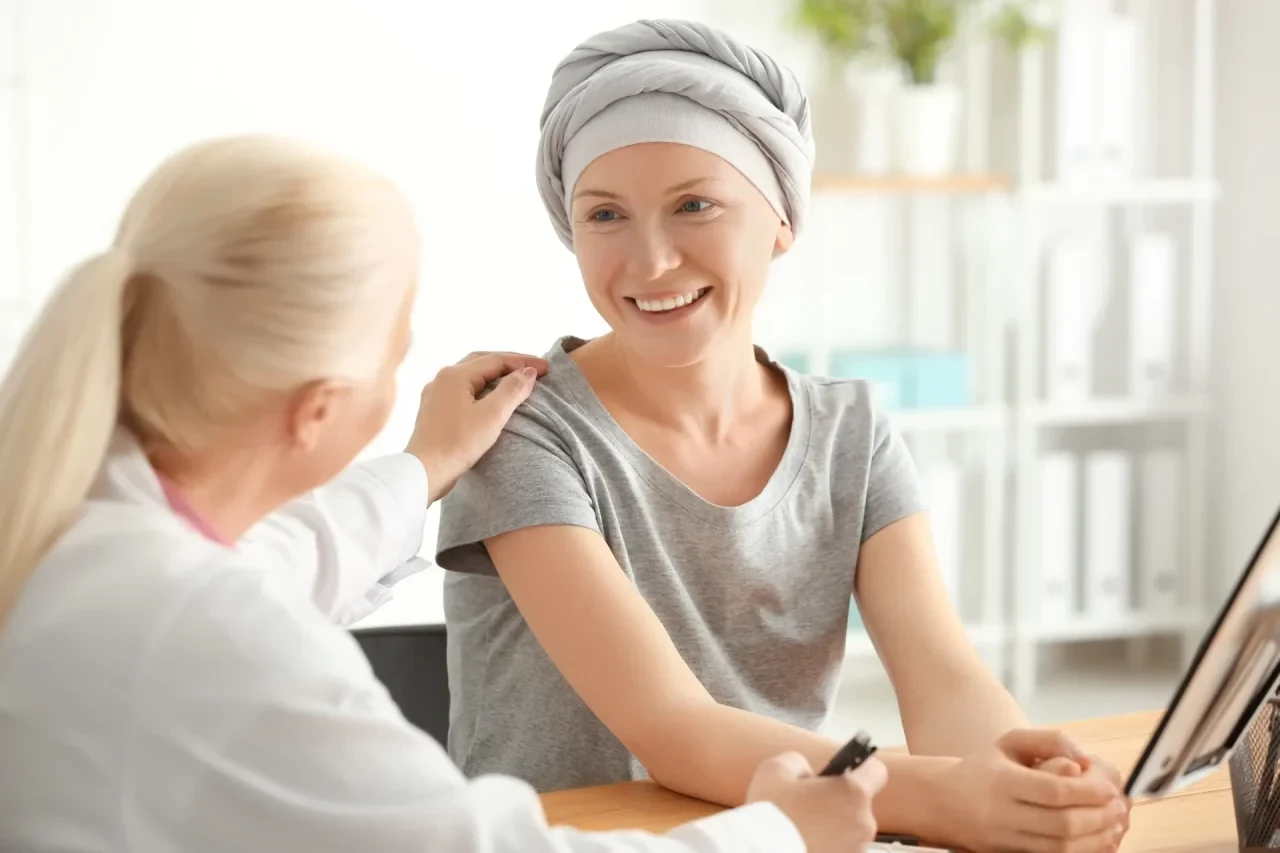 Onkologin legt einer Brustkrebspatientin mit Kopftuch beruhigend die Hand auf die Schulter – Beratungsgespräch zu Therapieoptionen und Nachsorge.