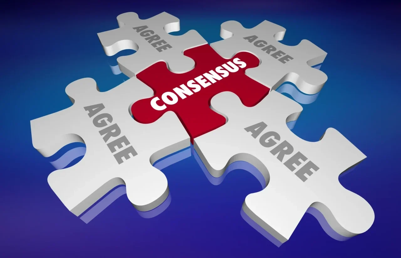Vier weiße Puzzleteile sind um ein rotes Puzzleteil mit der Aufschrift „CONSENSUS“ angeordnet. Die weißen Teile tragen jeweils das Wort „AGREE“. Blauer Hintergrund.