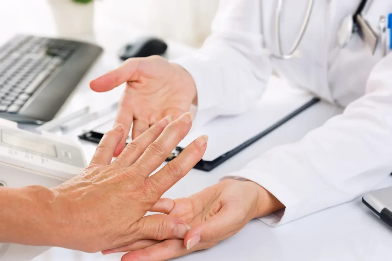 Eine Ärztin untersucht die Hände einer Person während einer rheumatologischen Sprechstunde in einer Praxis.