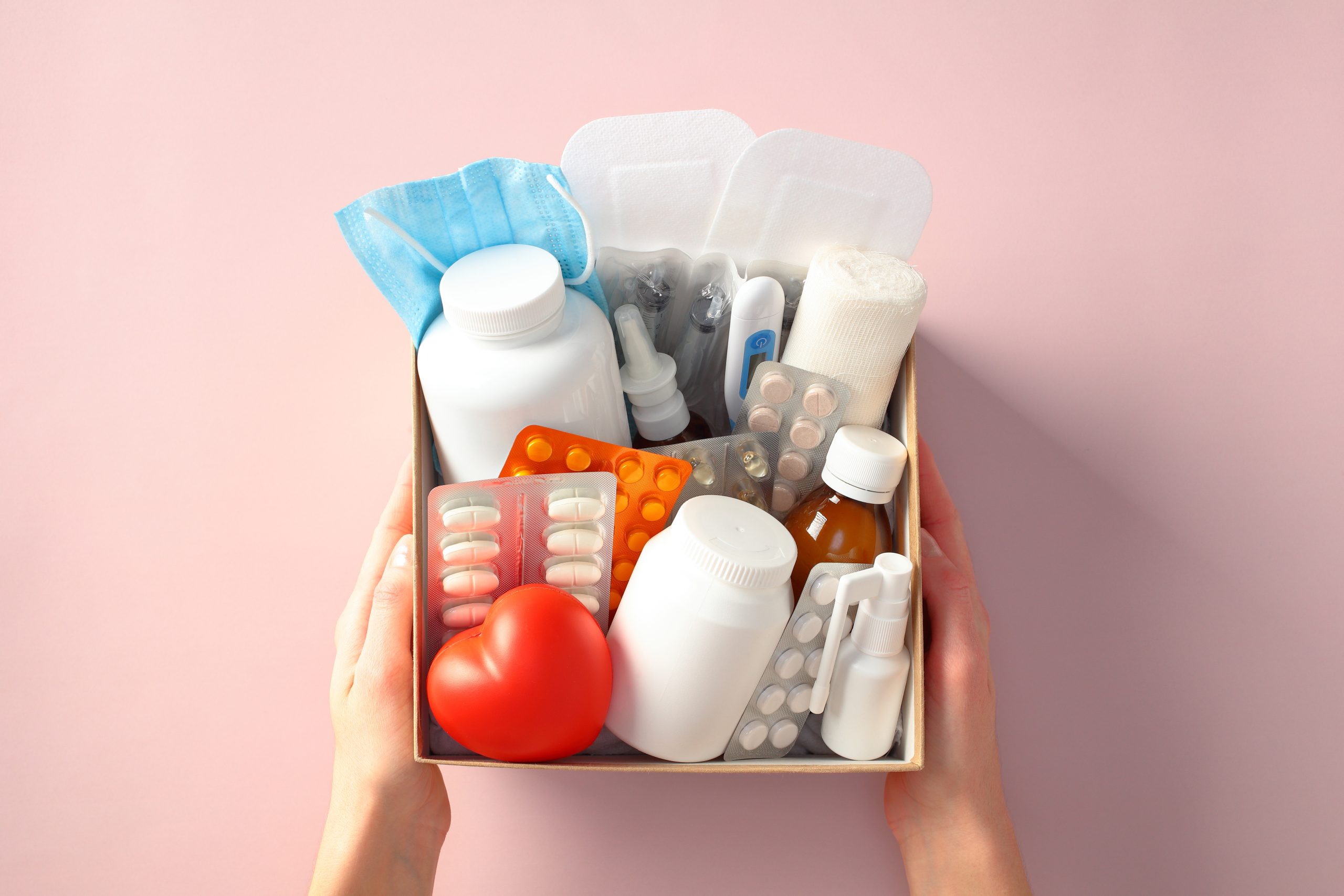 Box mit Grundausstattung wie Medikamente, Tabletten, Binde, Maske in Frauenhänden.