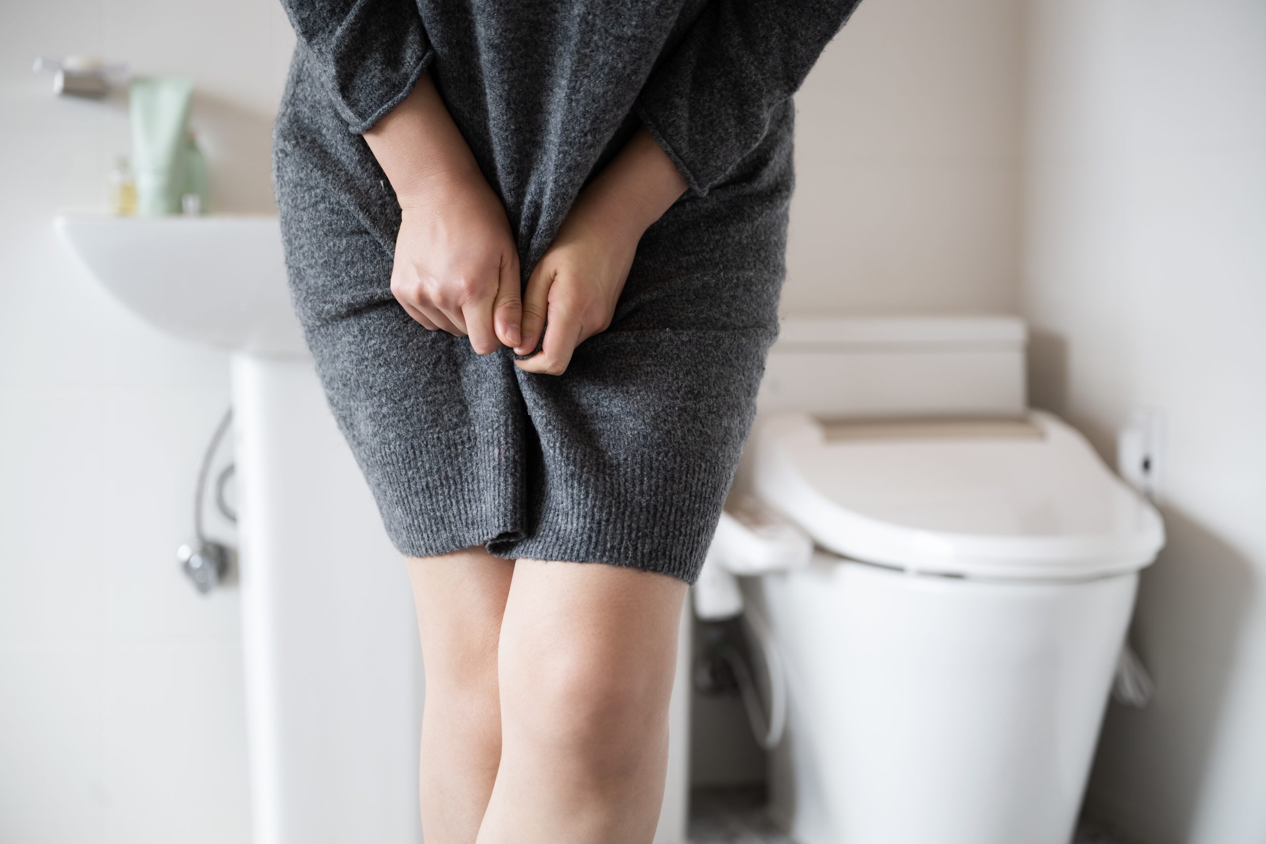 Frau im Bademantel auf der Toilette mit zusammengepressten Schenkeln.