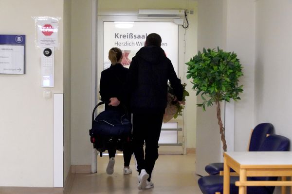 Frisch gebackene Eltern verlassen Kreißsaal mit Neugeborenem in der Babyschale.