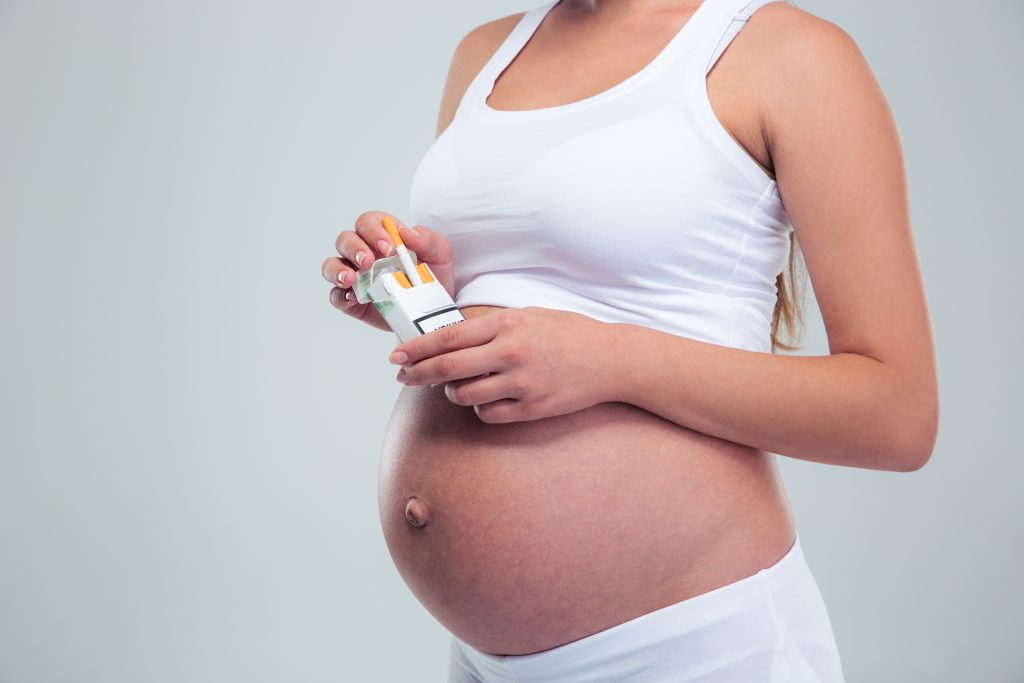 Schwangere Frau hält Zigarettenschachtel in der Hand