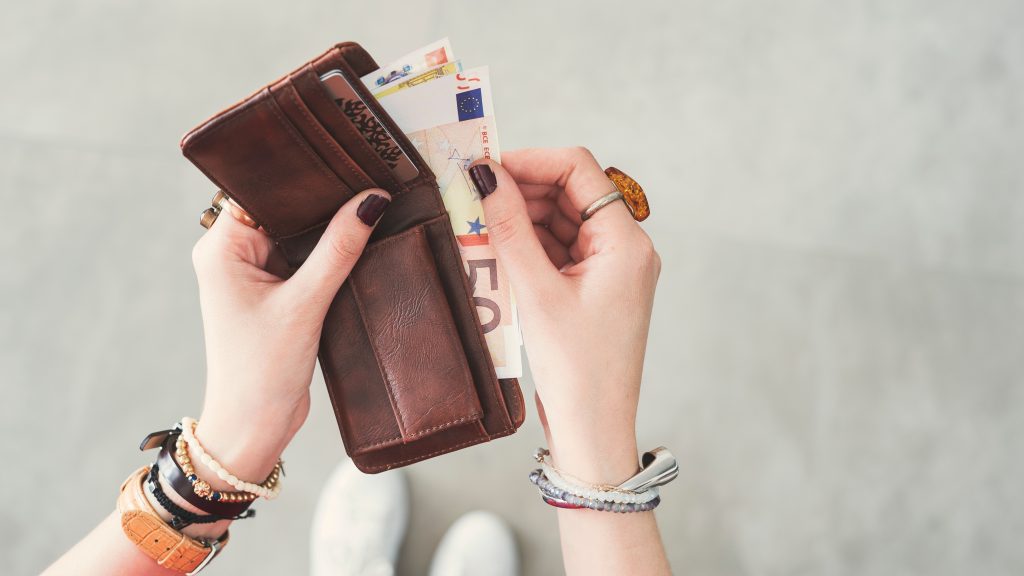 Frauenhände entnehmen ledernem Geldbeutel einen Geldschein