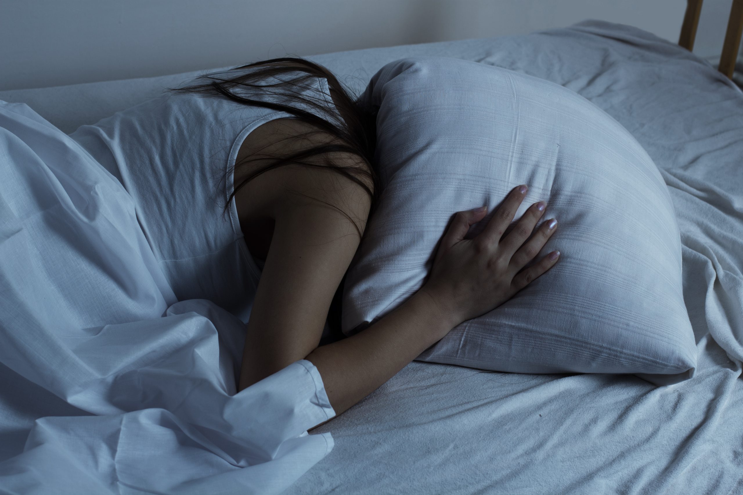 Frau im Bett hält sich Kissen über den Kopf