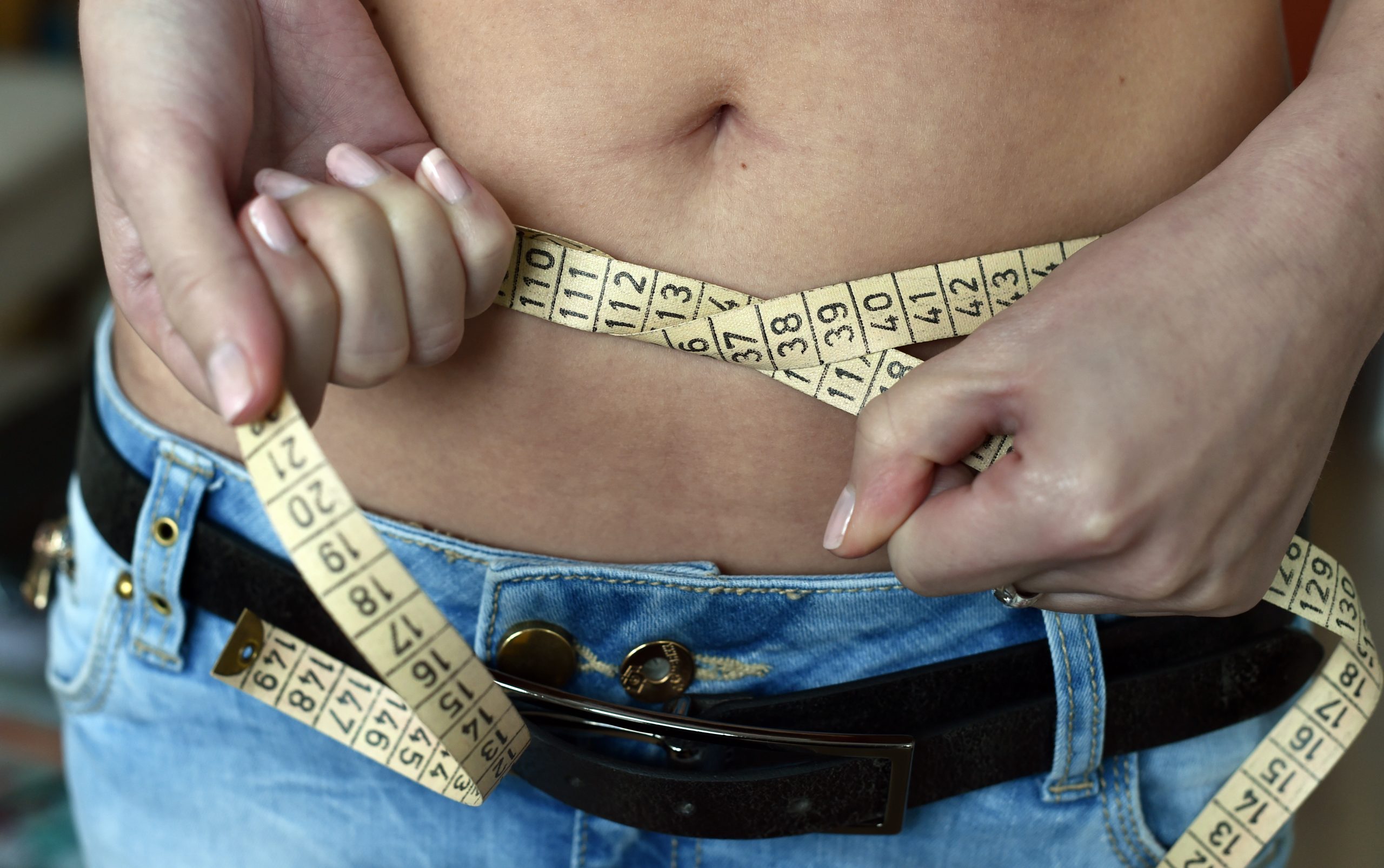 Eine junge Frau legt ein Maßband um ihren Bauch.