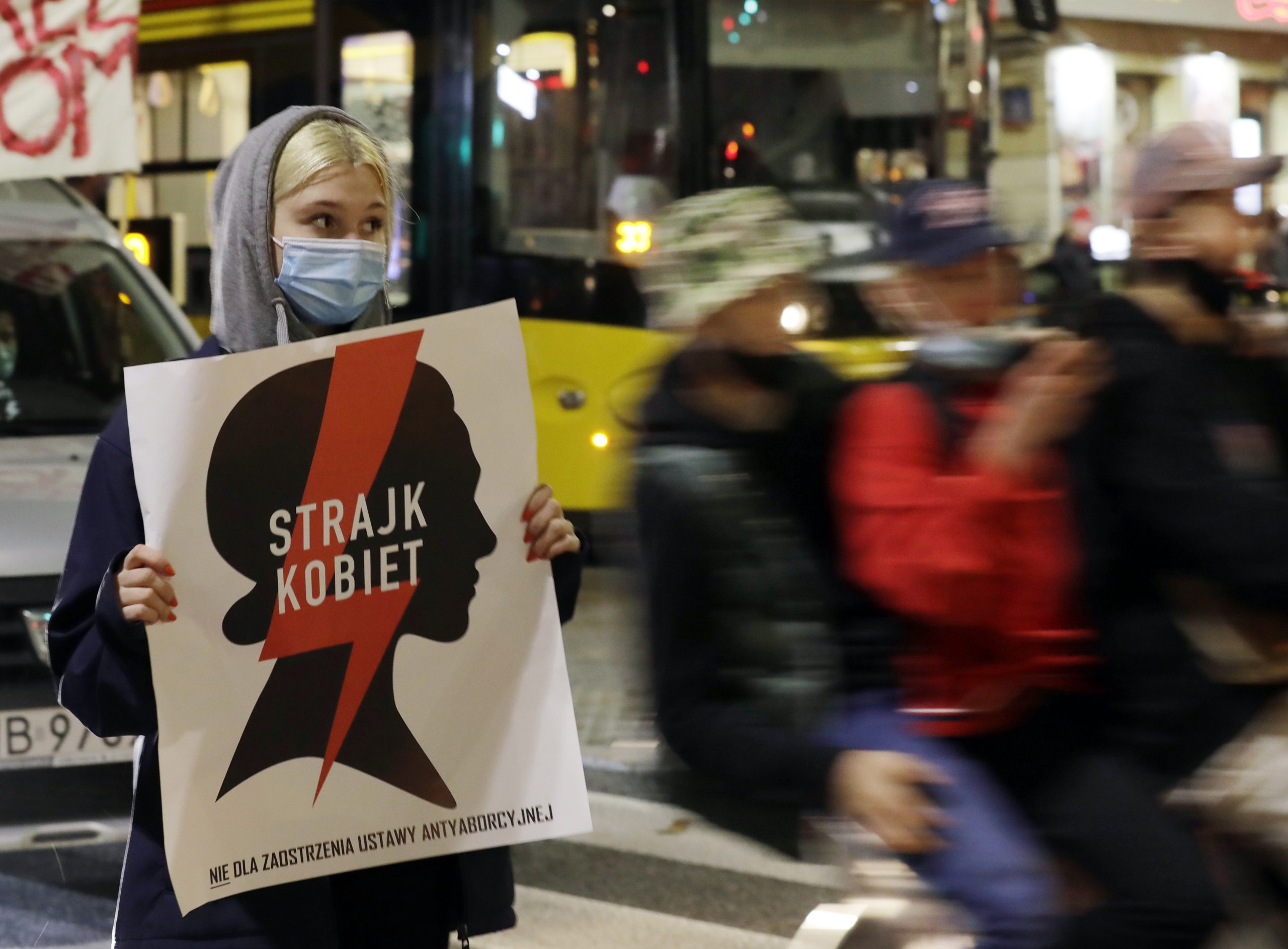 Maskierte Frau hält Protestschild in der Hand