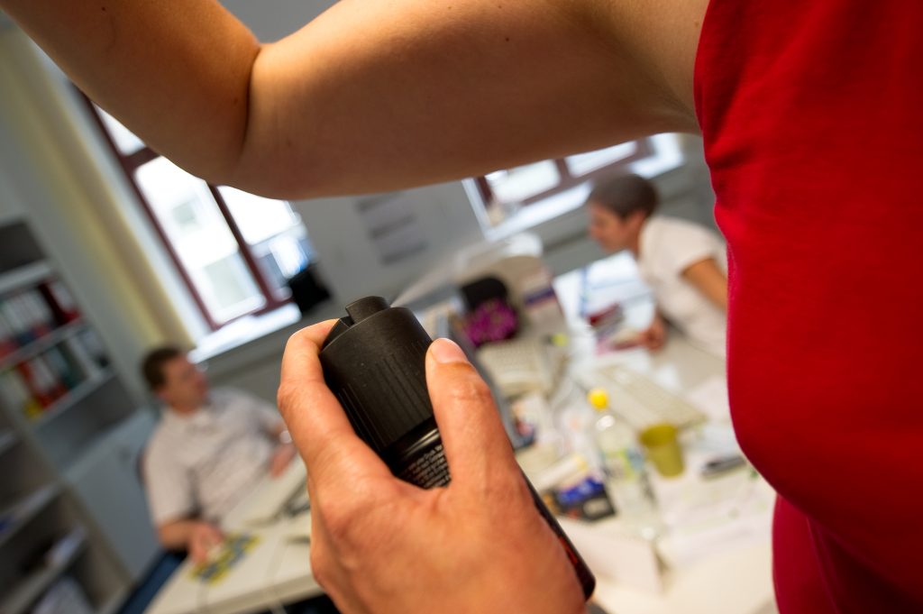 Eine Frau sprüht sich ein Deodorant in einem Büro unter die Achseln.