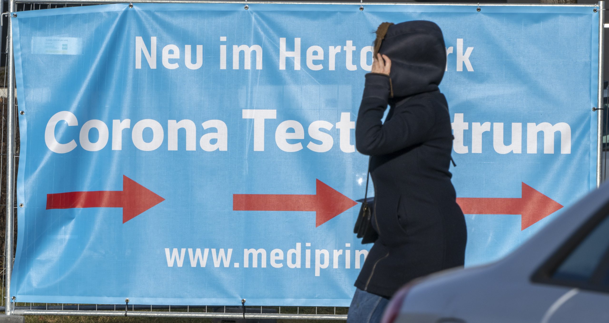 Eine Frau geht an einem Banner vorbei, das den Weg zu einem Corona-Testzentrum weist. Ermittler decken systematischen Betrug im Gesundheitswesen auf – besonders bei Corona-Testzentren und Pflegediensten