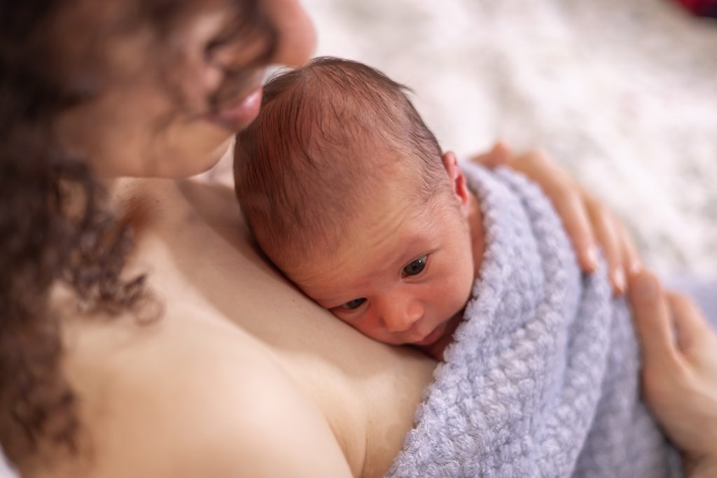 Adorable Newborn Baby Boy sitting on mother chest. Skin to Skin.