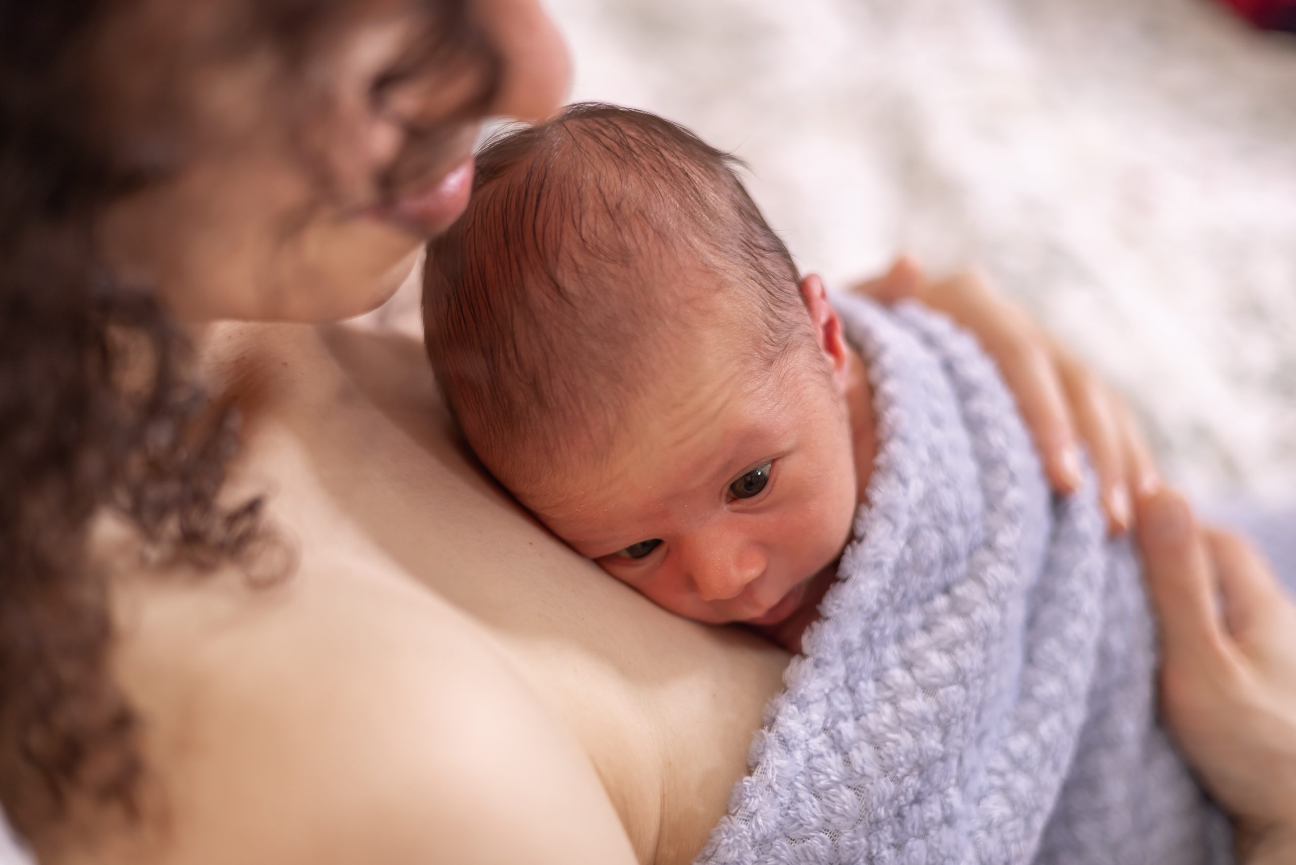 Adorable Newborn Baby Boy sitting on mother chest. Skin to Skin.