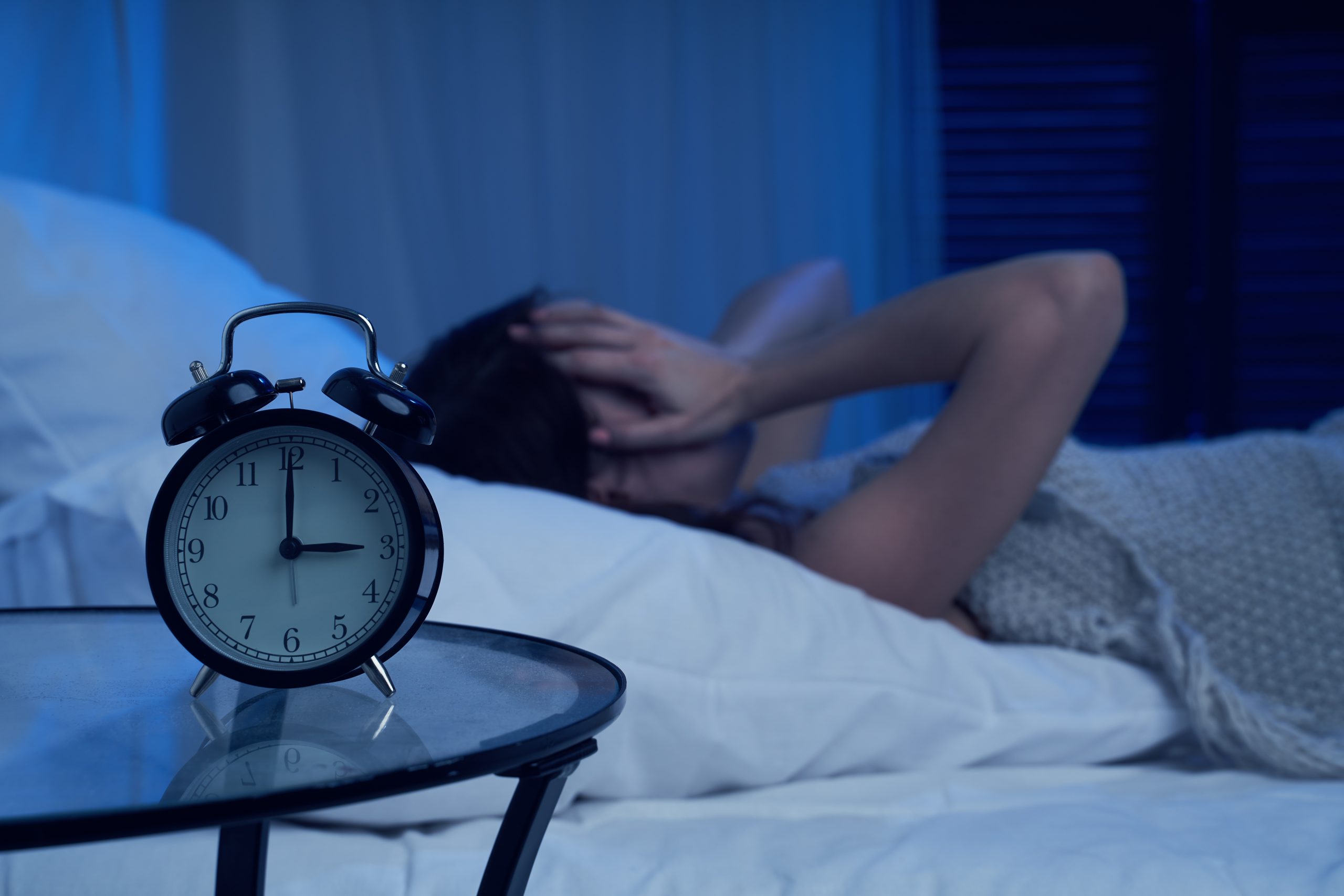 Woman with insomnia lying on bed next to alarm clock at night in apartment
