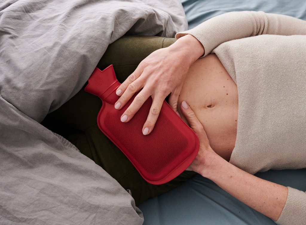 ILLUSTRATION - Eine Frau hält sich eine Wärmflasche an den Unterbauch, während sie im Bett liegt. (gestellte Szene) Viele Betroffene der Unterleibserkrankung Endometriose leiden unter starken Symptomen und damit verbundenen Einschränkungen im Alltag. (Zu dpa: "Mysterium Endometriose - Wenn die Periode zur Qual wird")
